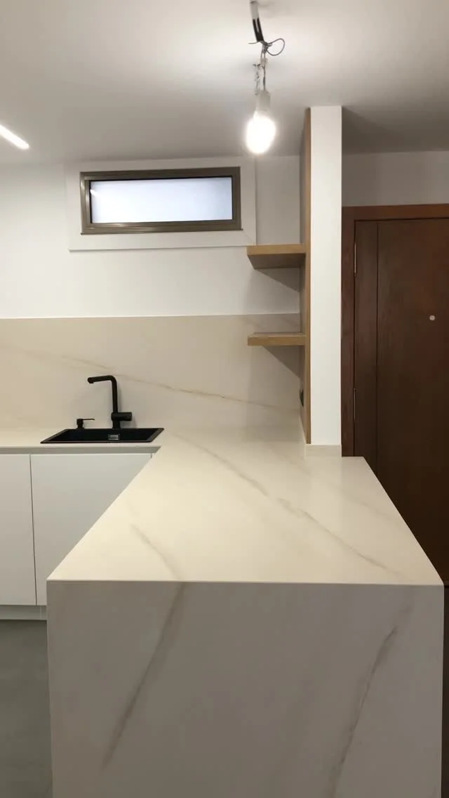 Cocina blanca con encimera clara y grifería negra, publicada por Reformas Casal